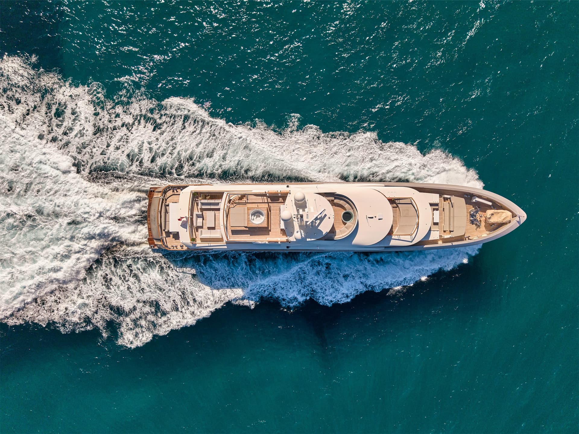 Aerial view of a large white yacht speeding through deep turquoise ocean water creating white wake.