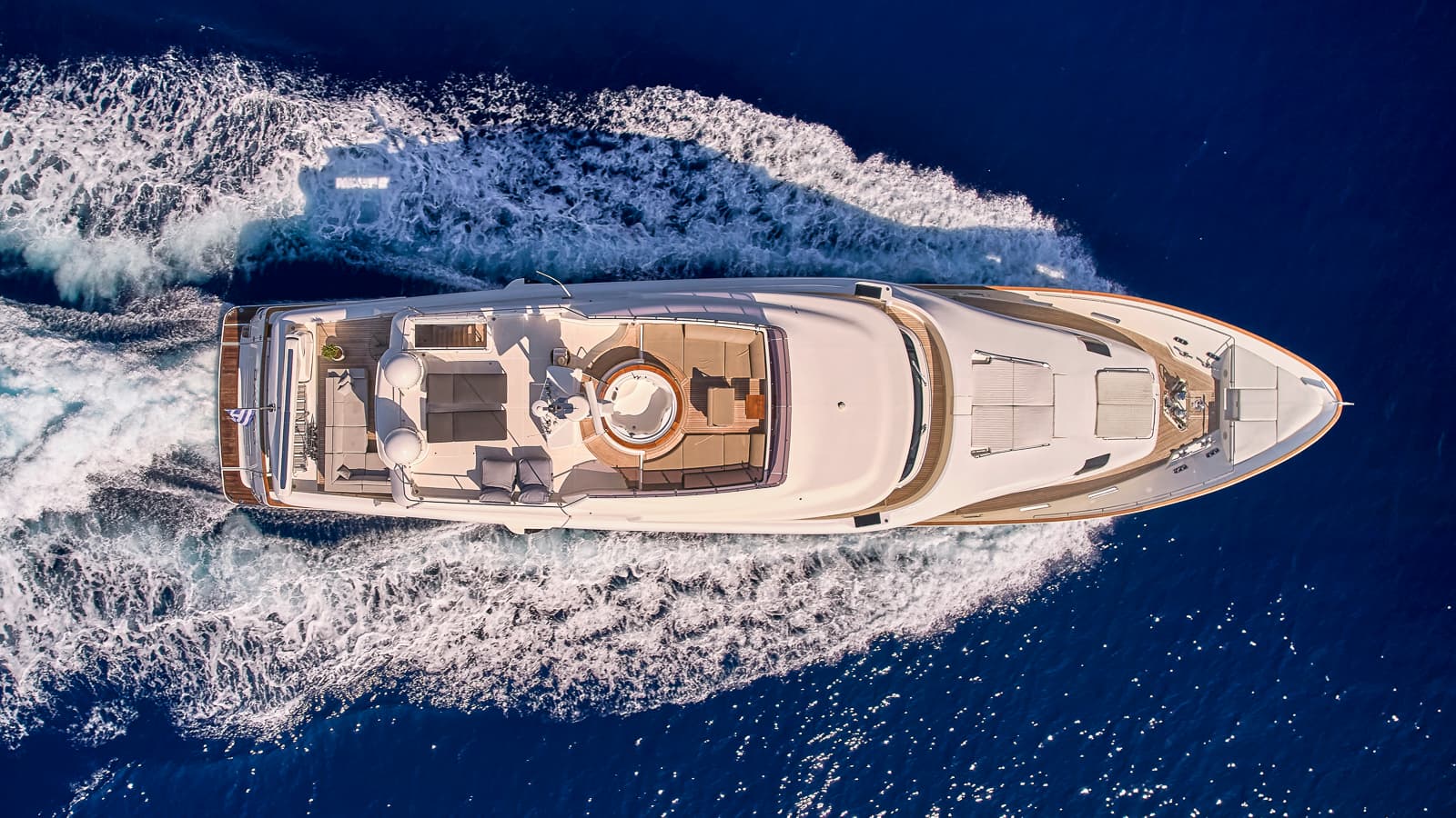 Luxury yacht with hot tub speeding across deep blue sea, Greek flag visible