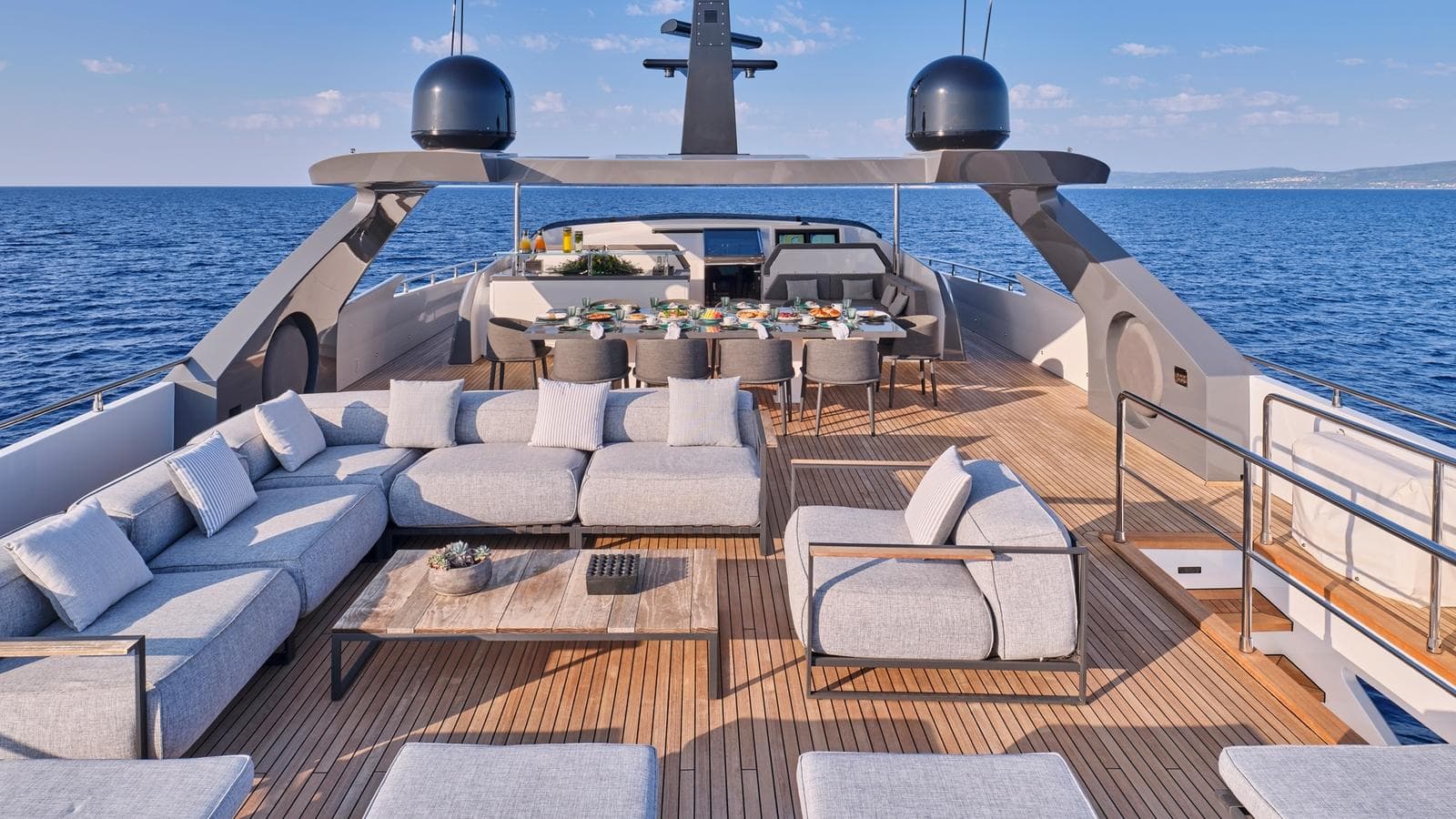 Luxury yacht deck with grey outdoor seating, dining table, and blue sea in background