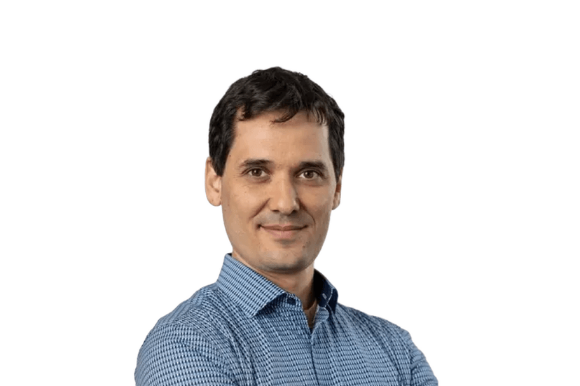 Portrait of a man with dark hair wearing a blue patterned button-down shirt against a white background.