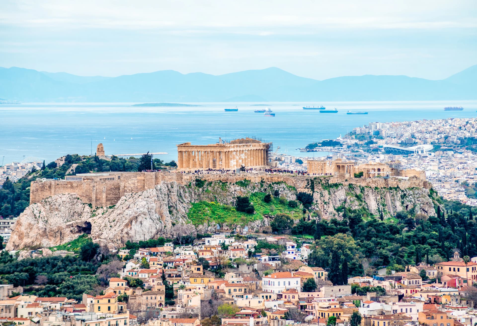 View of the Acropolis of Athens (in Greece) with Filopappos Hill, the Saronic gulf and the port of Piraeus in the background.