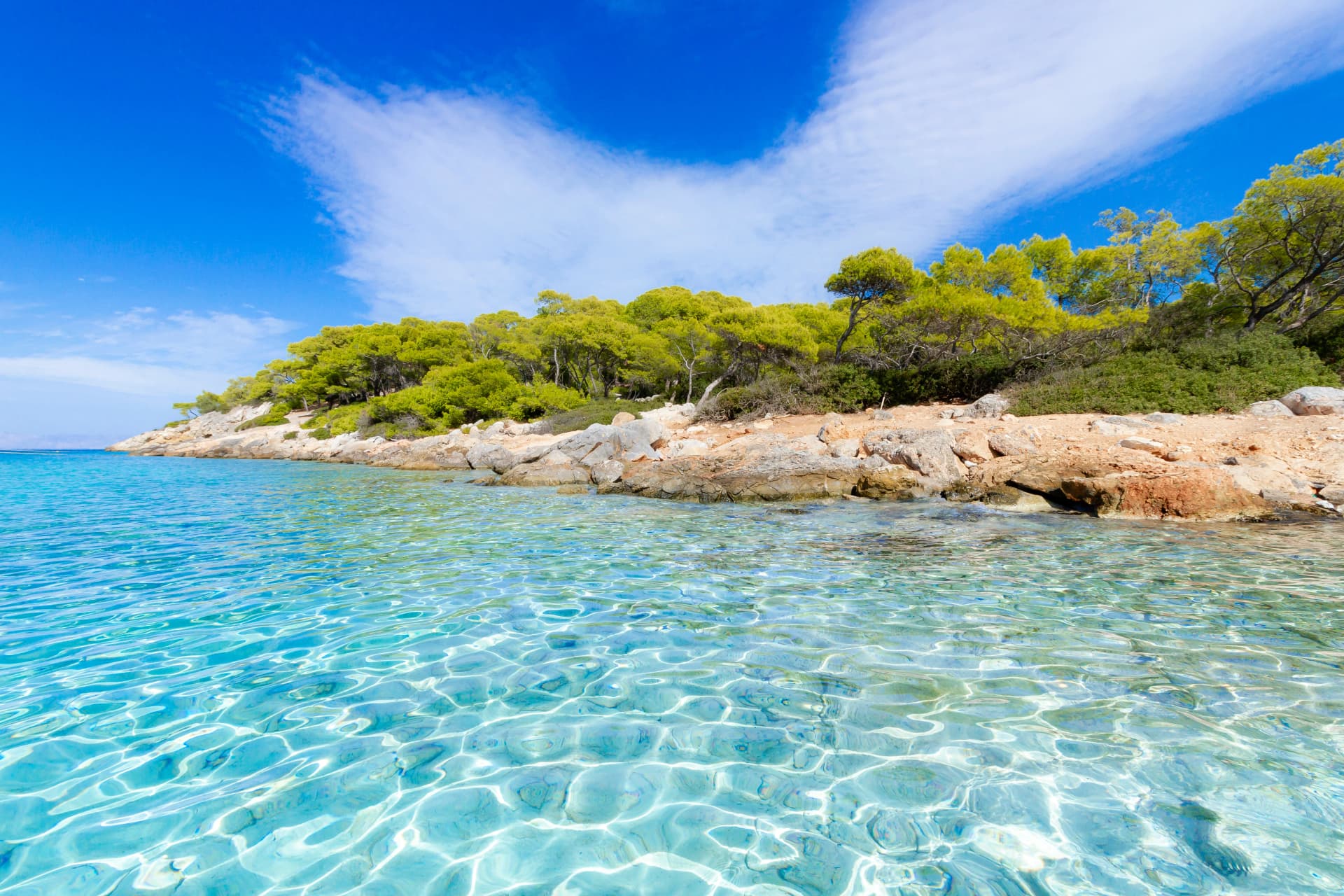 Aponissos beach, a pristine shore at the island of Agkistri, Greece, where turquoise waters meet with the green forest and the clear blue sky.