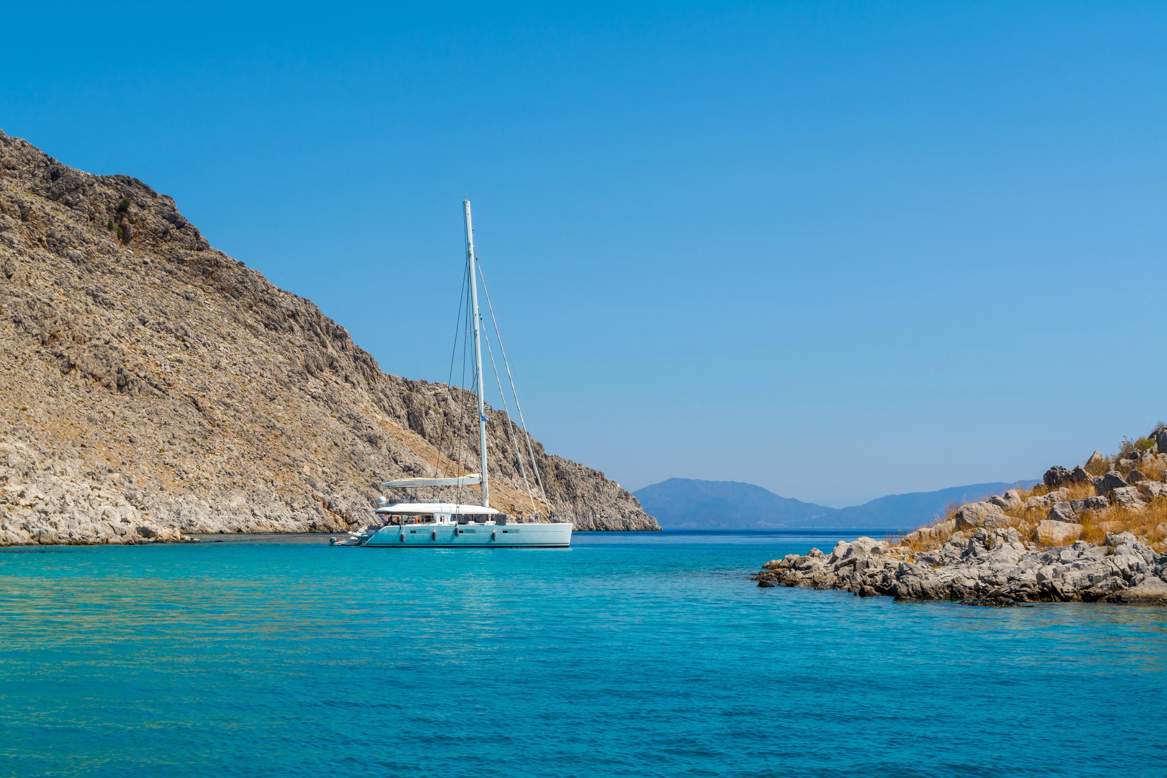 Yacht Boat Catamaran On Turquoise Sea In Bay Near Symi Greece. Sailing Travel Vacation Background
