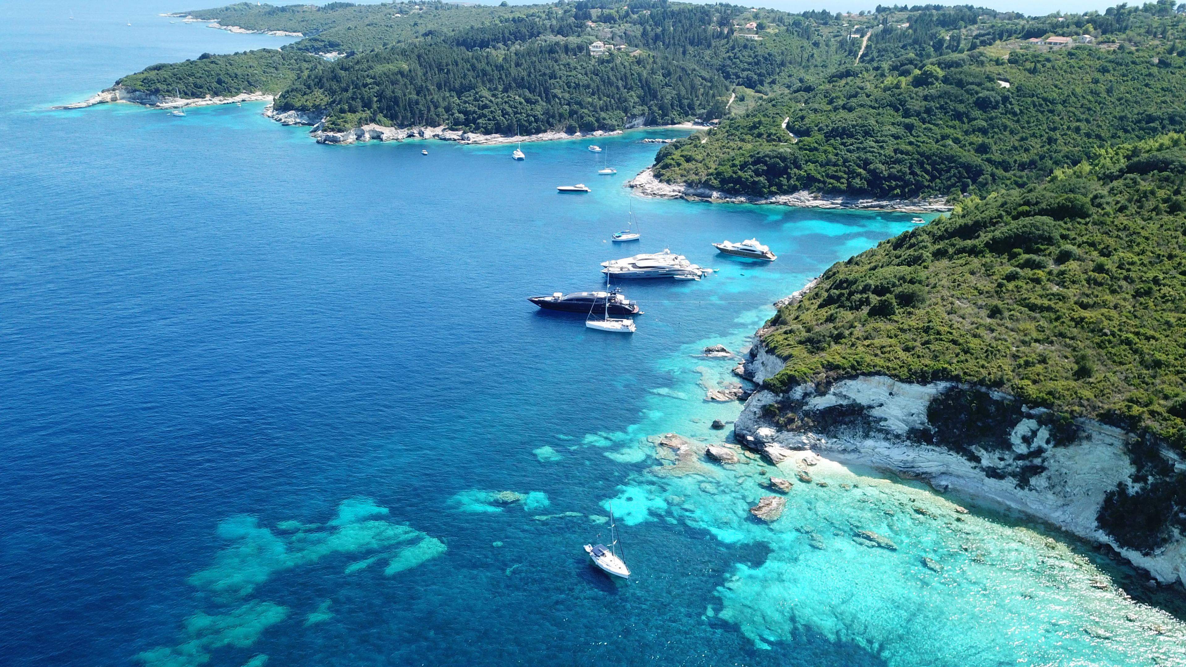 Aerial drone photo of tropical paradise turquoise beach of Voutoumi with sail boats docked in island of Anti paxos, Ionian, Greece