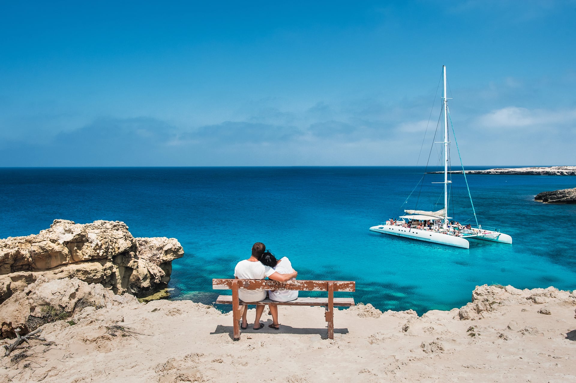 Loving couple sitting on a bench and looks at the lagoon. Honeymoon lovers. Man and woman on the island. Couple in love on vacation. A voucher for a cruise trip. Sea tour. Honeymoon trip. Cruise ship