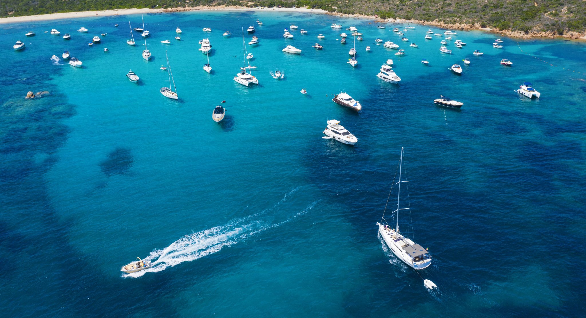 View from above, stunning aerial view of a beautiful bay full of boats and luxury yachts. A turquoise sea bathes the green and rocky coasts. Liscia Ruja, Emerald Coast Sardinia, Italy