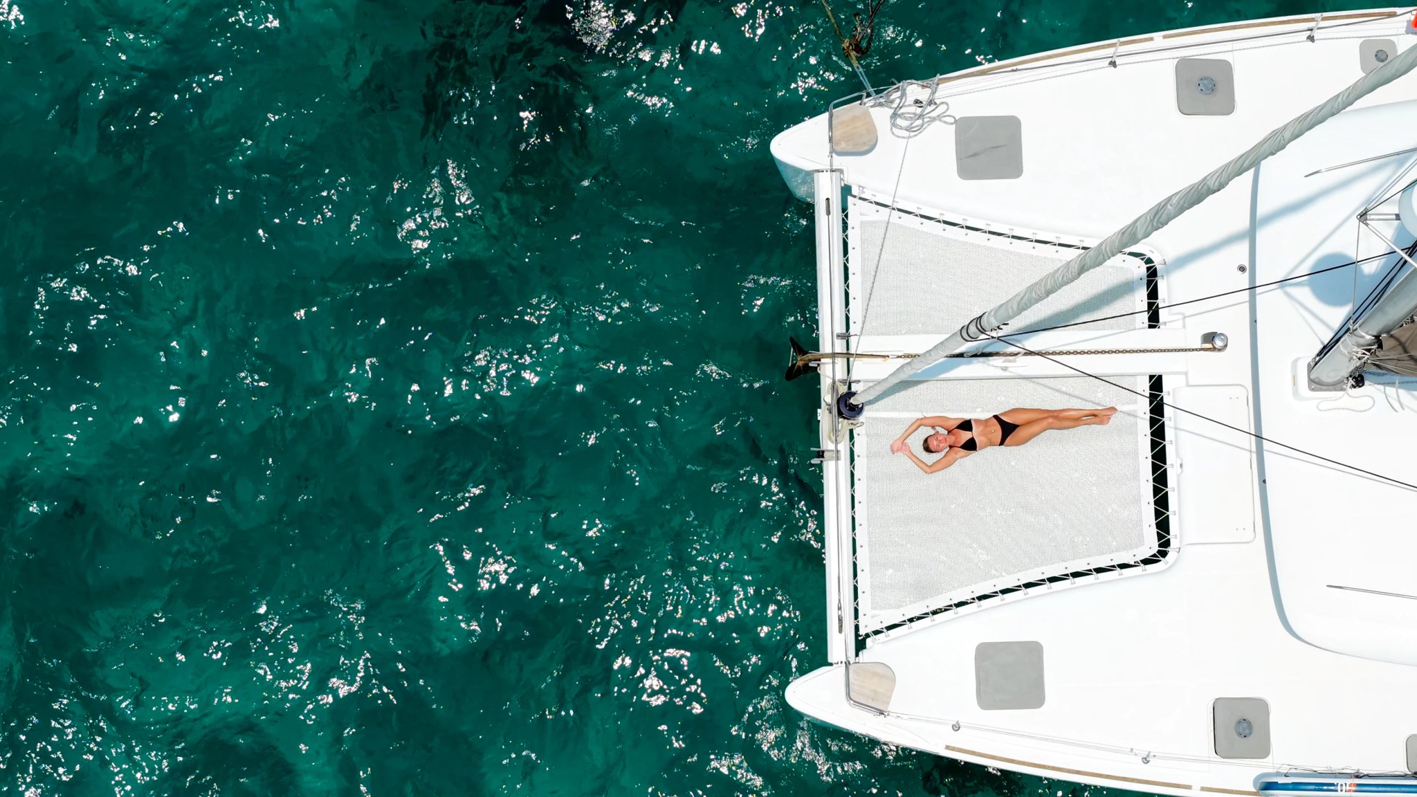 Slender woman on a yacht. Beautiful white woman sunbathing on the bow of a snow-white sailing yacht in the tropics. Yachting concept in a hot country. Holidays on a catamaran.